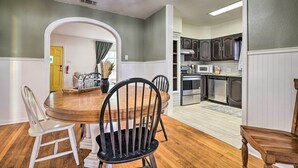 Un comedor con mesa y sillas de madera, una cocina al fondo y un pasillo que lleva a otra habitación.