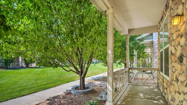 A covered porch with stone walls, a tree, and a well-maintained lawn.