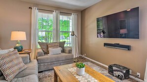 A living room with a sofa, a coffee table with a plant, a lamp, and a TV mounted on the wall.