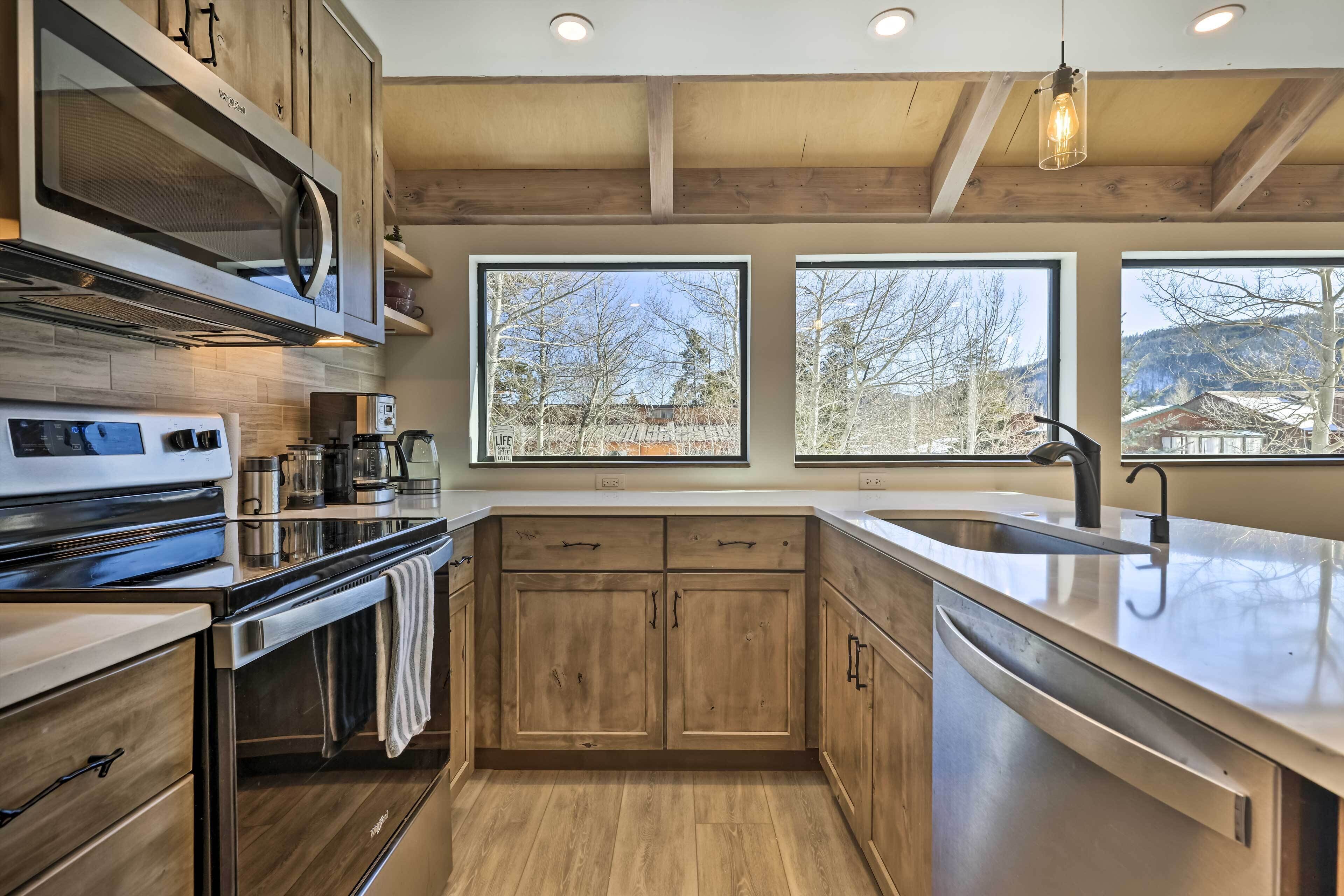 A modern kitchen with wooden cabinets, stainless steel appliances, and large windows offering views of the outdoors.