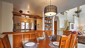 Uma área de refeições com mesa de madeira posta para quatro pessoas, rodeada por cadeiras, e um lustre pendurado acima.