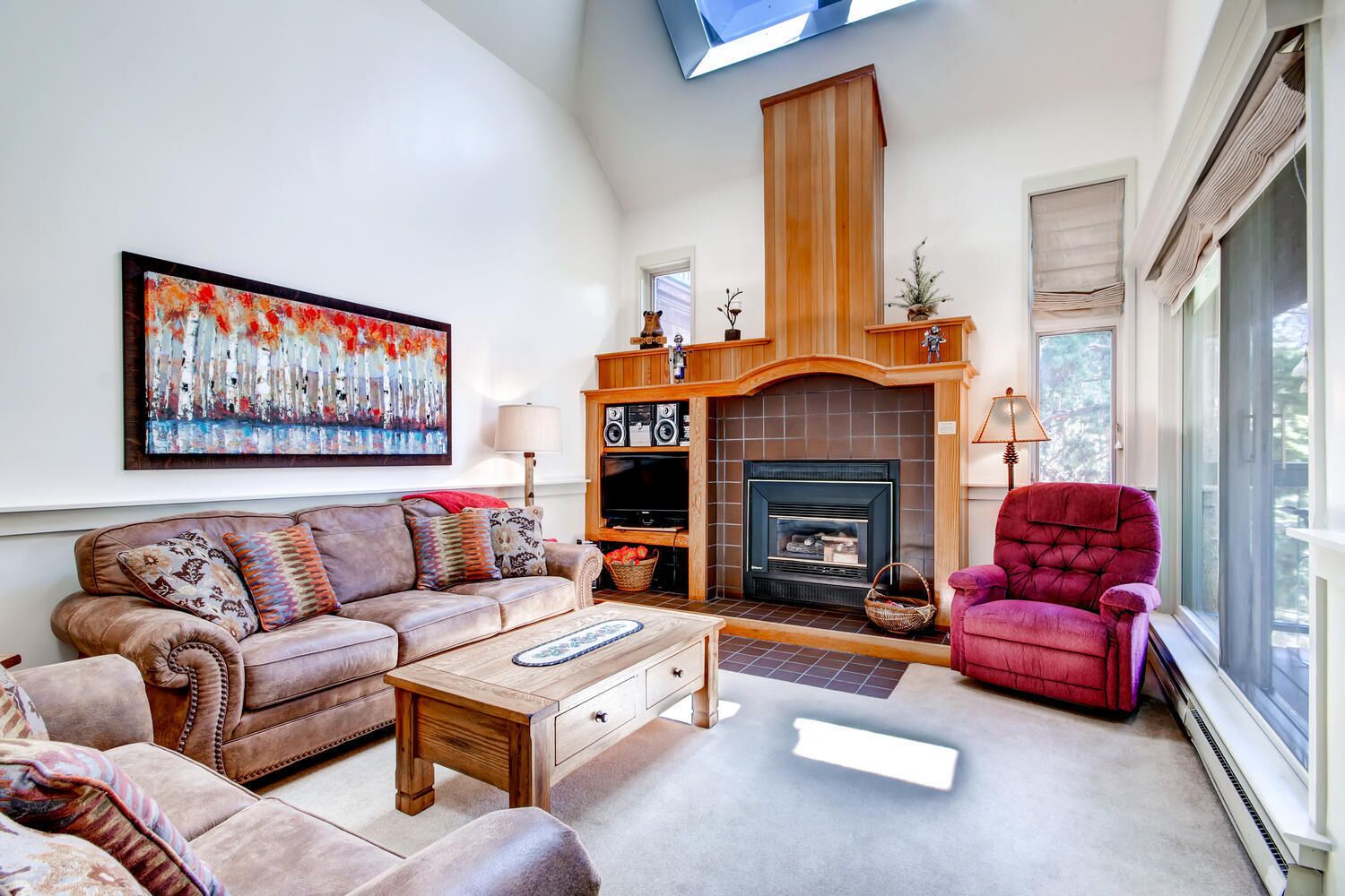 A living room with a fireplace, a sofa, a red armchair, and a large painting on the wall.