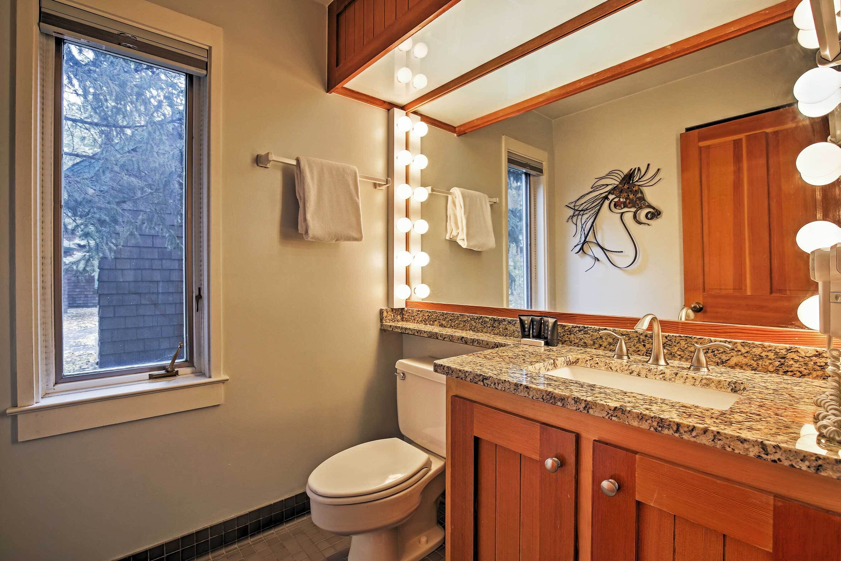 Une salle de bain comprenant un meuble-lavabo, un lavabo et un miroir avec éclairage, des toilettes et une fenêtre.