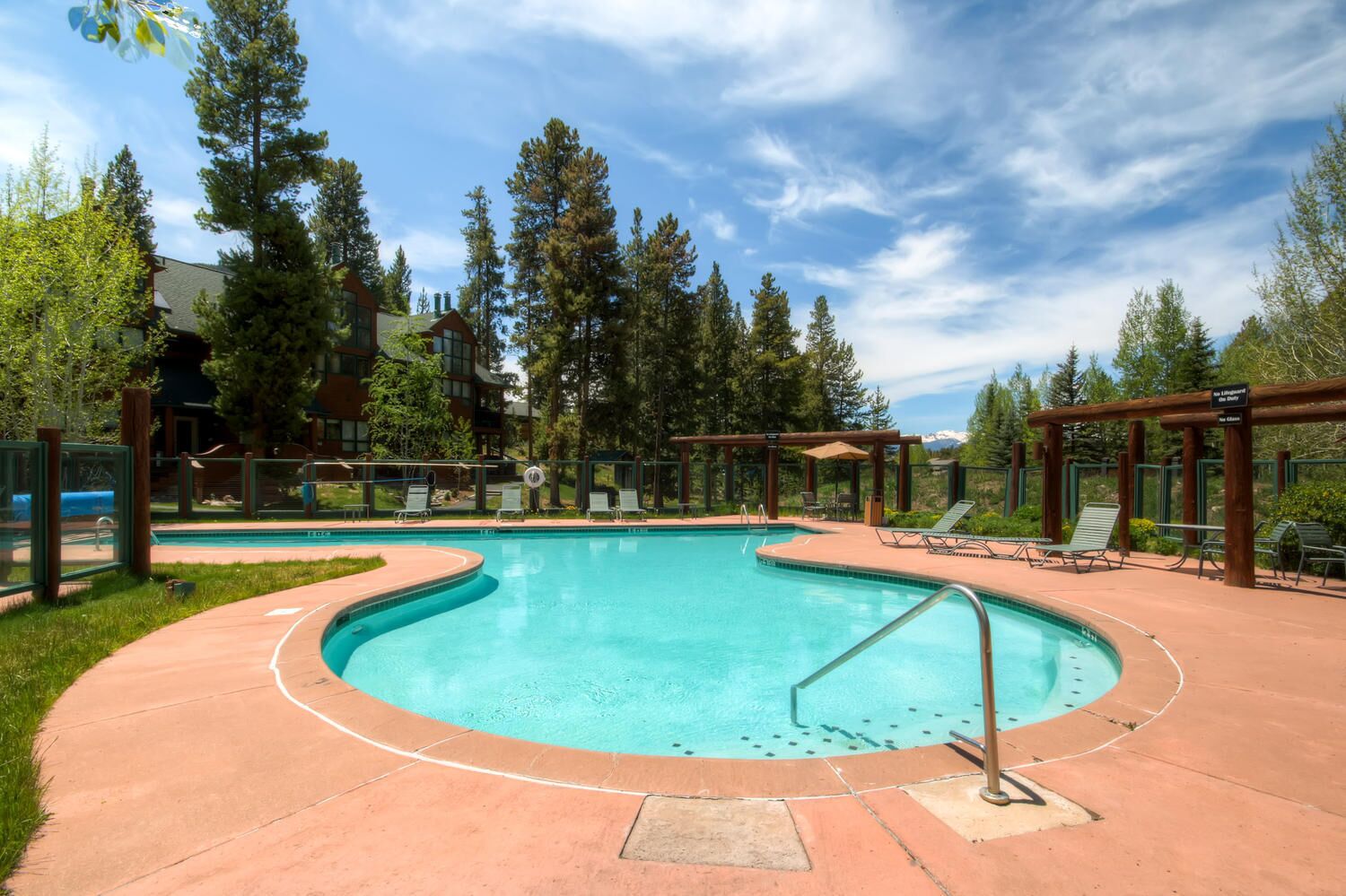 A swimming pool with a curved design, surrounded by lounge chairs and a wooden pergola.