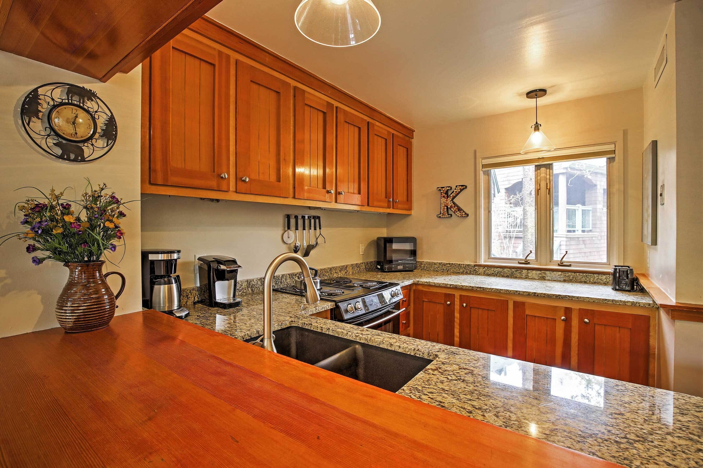 A kitchen with wooden cabinets, granite countertops, a stainless steel sink, a stove, and a coffee maker.