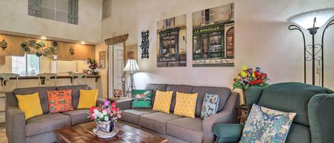 A cozy living room with a grey sofa, a wooden coffee table, and a green armchair. There are decorative pillows and wall art depicting Parisian cafes.