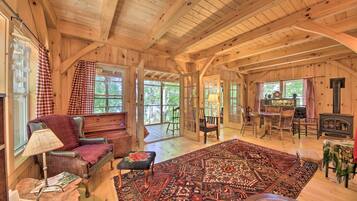 A cozy cabin interior with a large wooden ceiling, a fireplace, a dining area, and a seating area with a rug and a bench.