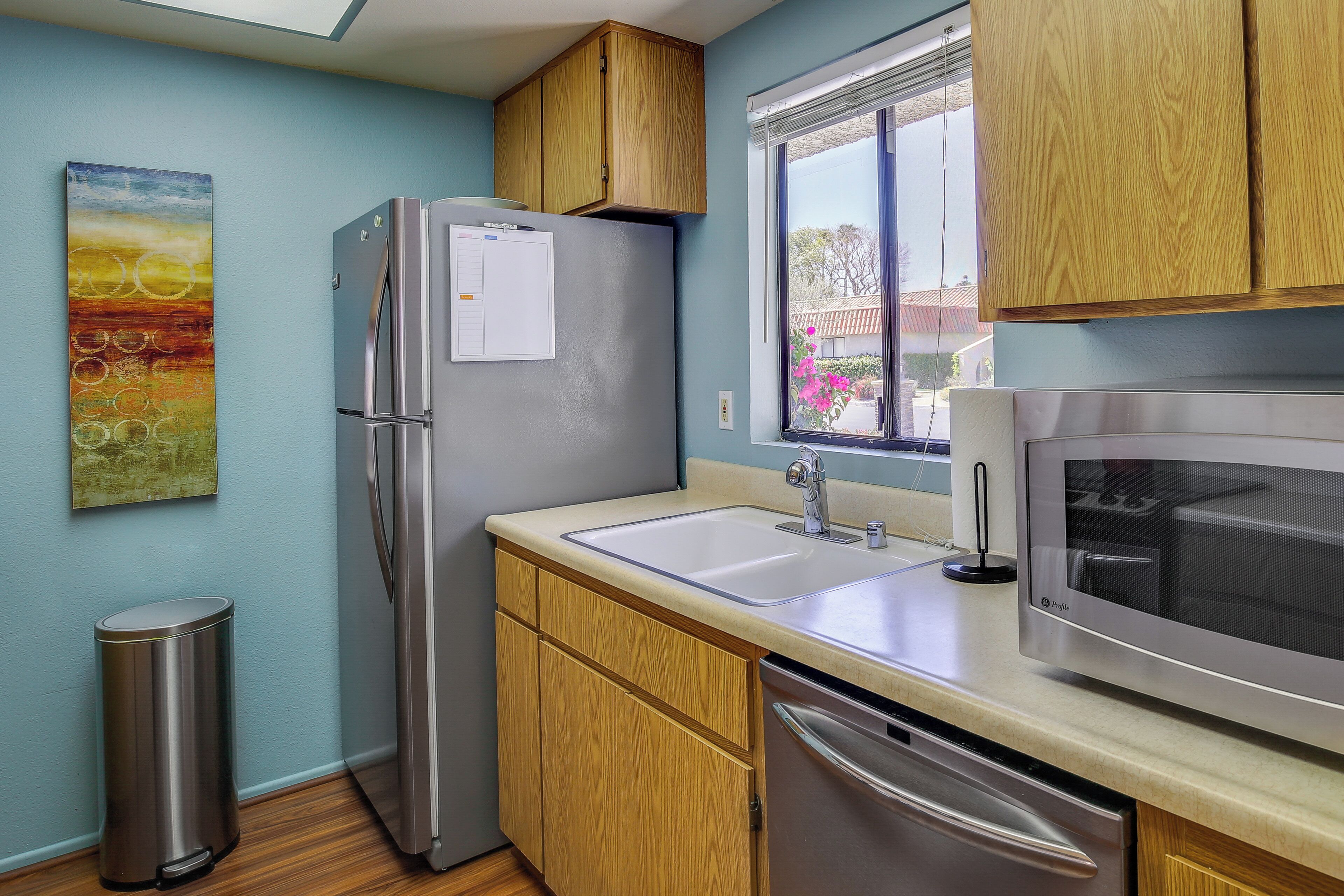 Una cocina con armarios de madera, un refrigerador de acero inoxidable, un lavamanos y un microondas.