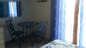 A bedroom with a bed, a small round table, two chairs, a TV mounted on the wall, and a window with curtains.
