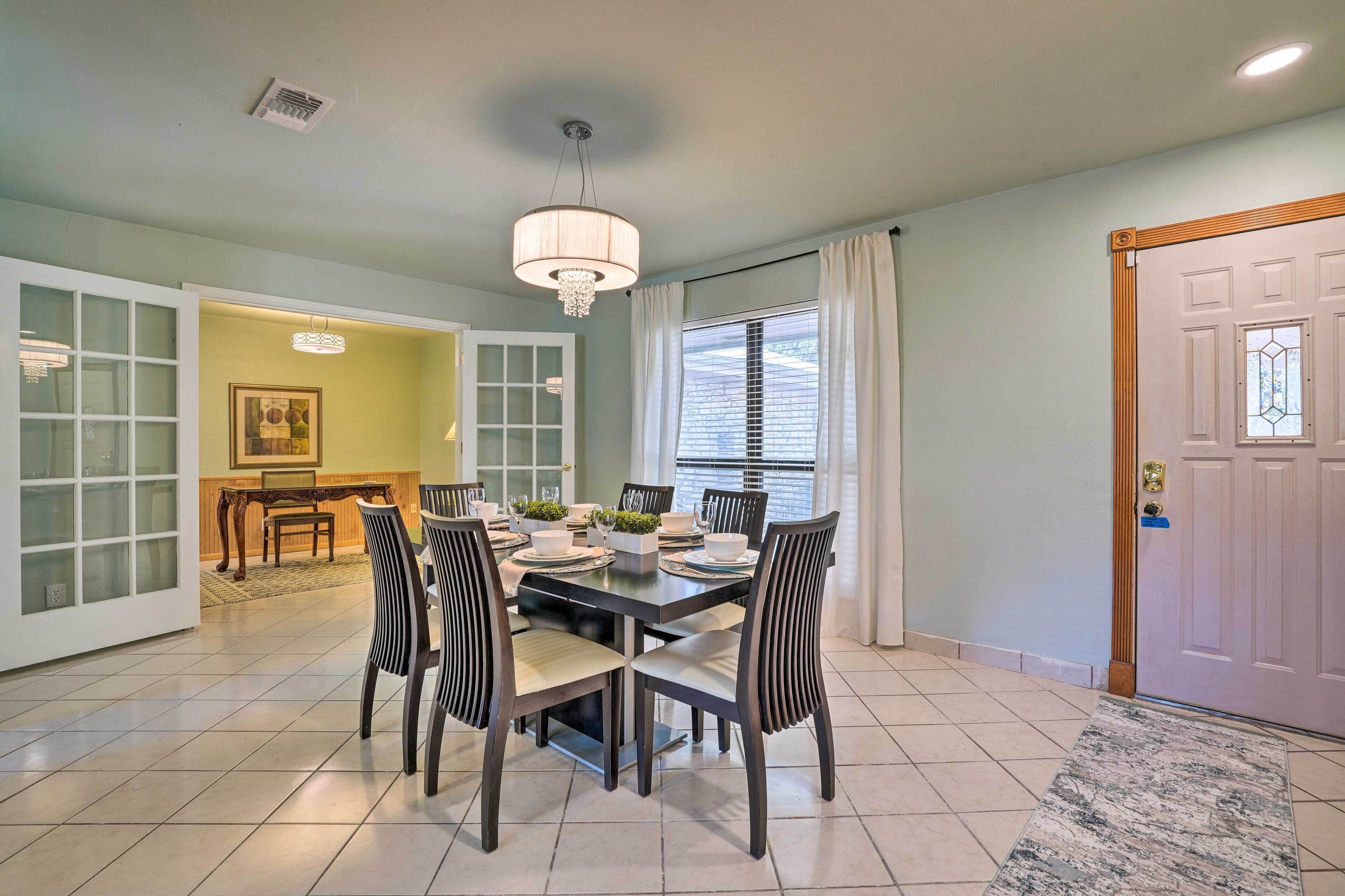 A dining area with a table set for four, surrounded by chairs, a chandelier, and a window with blinds.