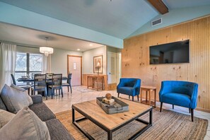 A living room with a sofa, coffee table, blue armchairs, and a TV mounted on a wooden wall.