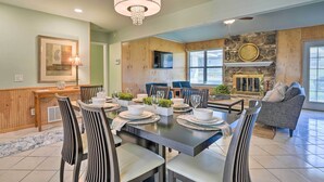 A dining area with a long table set for six, surrounded by striped chairs, a chandelier, and a stone fireplace.