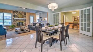 A spacious living room with a stone fireplace, a dining area with a large table and chairs, and a kitchen visible through an open door.