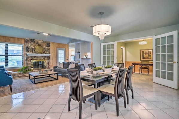 A spacious living room with a stone fireplace, a dining area with a large table and chairs, and a kitchen visible through an open door.