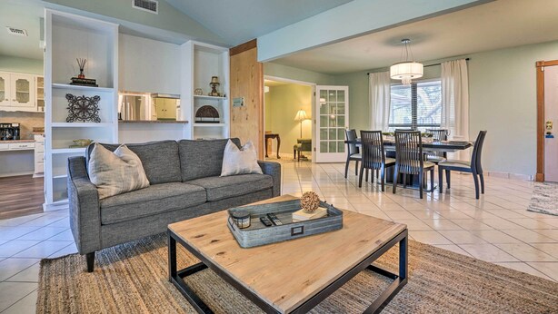 A spacious living room with a grey sofa, a coffee table with decorative items, and a dining area with a chandelier.