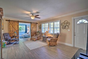 A spacious living room with a large sliding barn door, a ceiling fan, and a view through the windows.