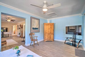 A spacious living room with a ceiling fan, wooden cabinet, TV stand, and a chair.