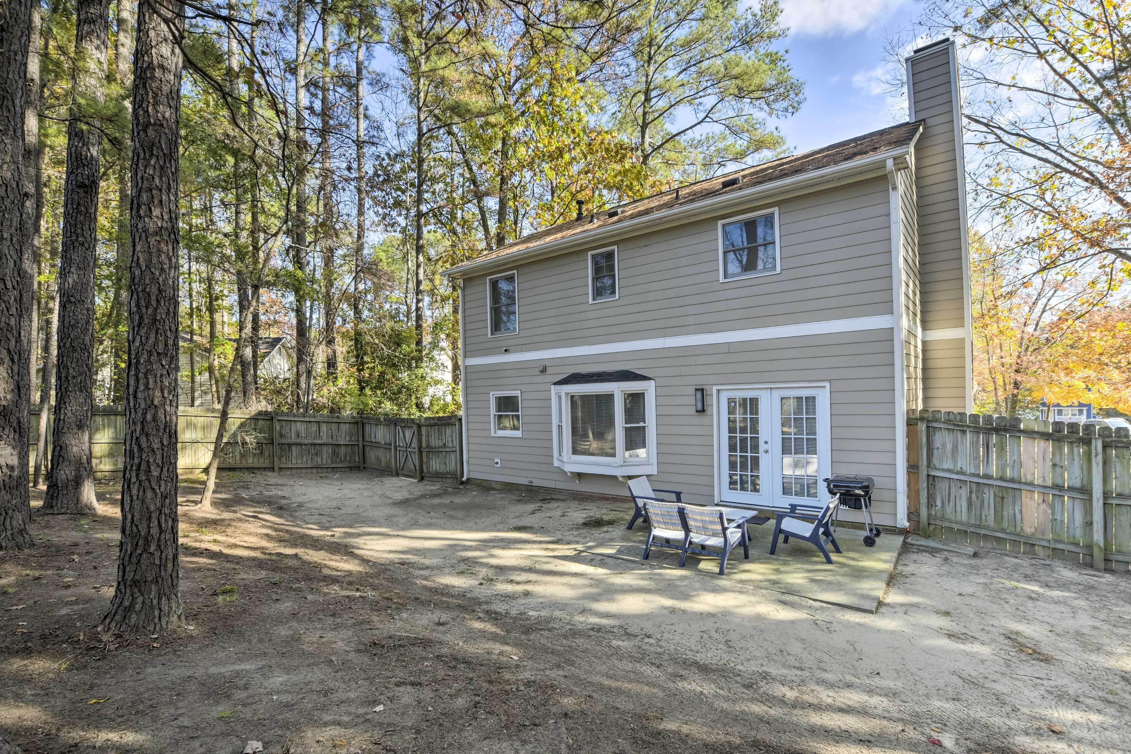 A two-story house with a fenced backyard, a patio with a table and chairs, and a chimney.