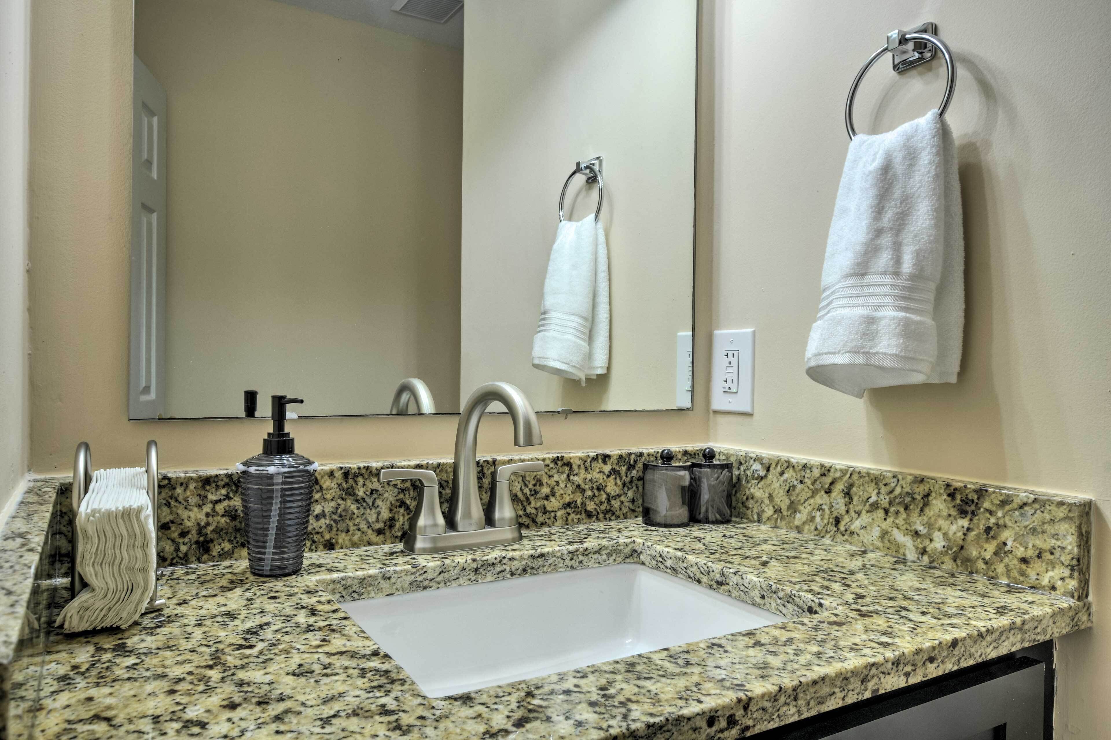Un baño con encimera de granito, un lavabo blanco, un espejo, un perchero para toallas y un dispensador de jabón.