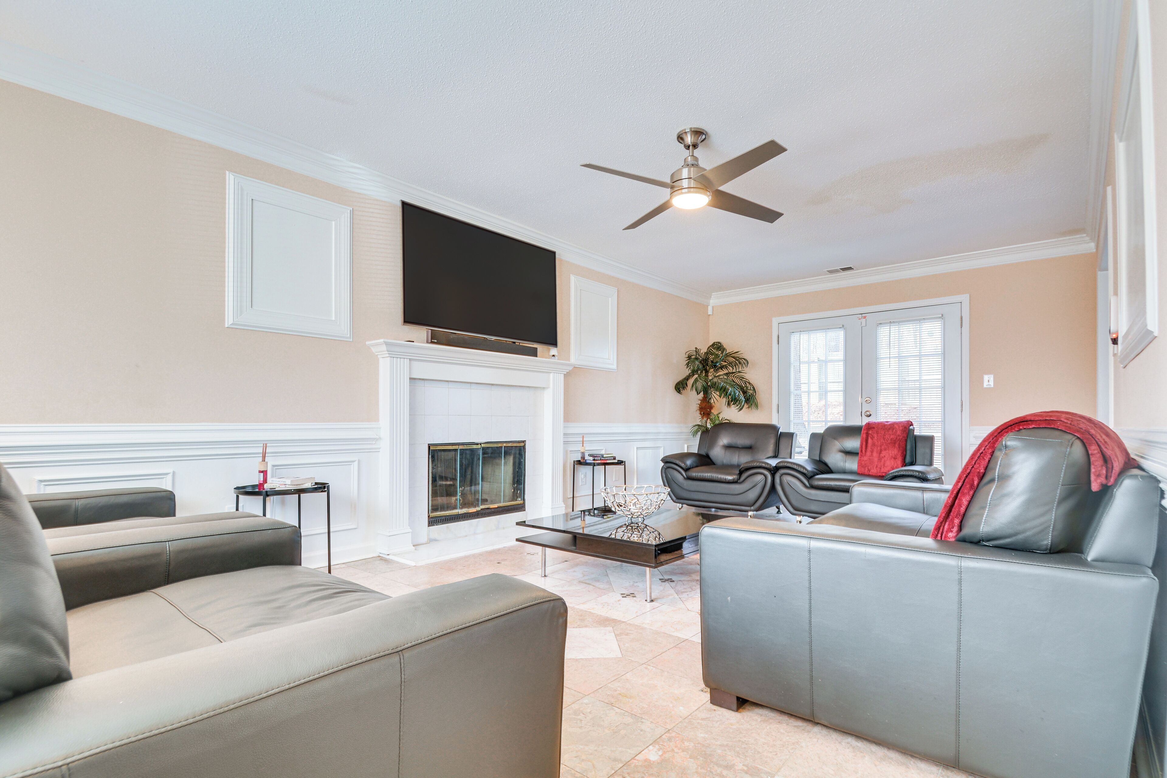 A living room with a fireplace, leather sofas, a flat-screen TV, and a ceiling fan.
