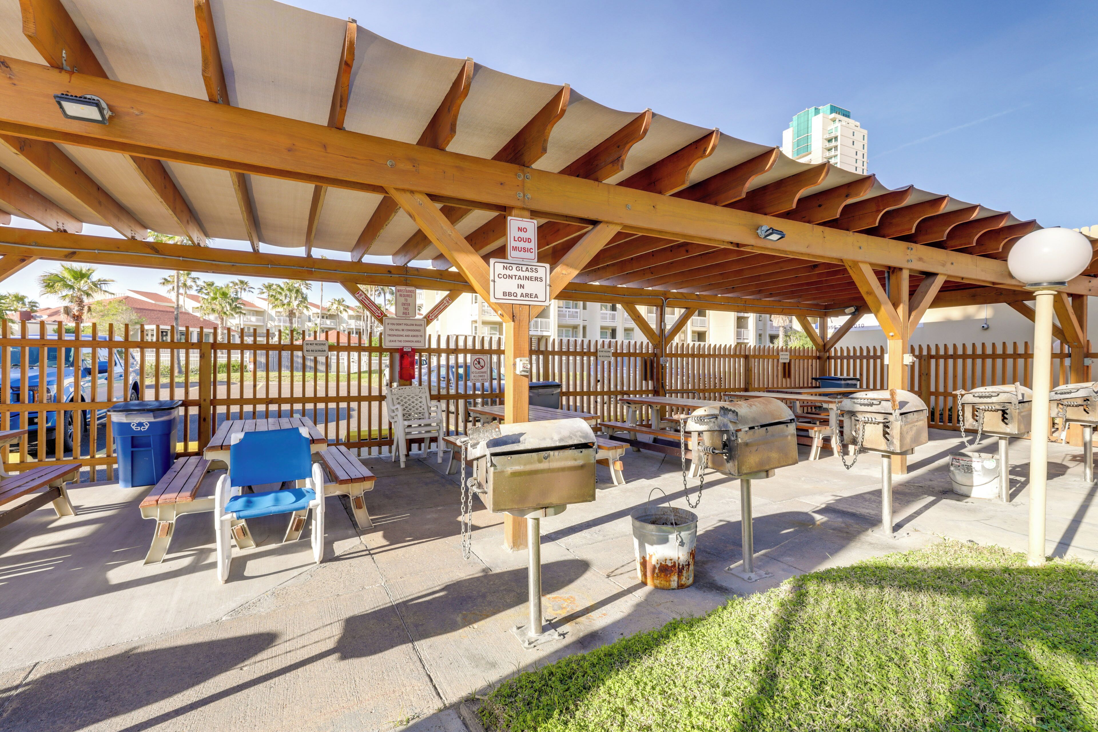 An outdoor patio with wooden tables, chairs, and barbecue grills.