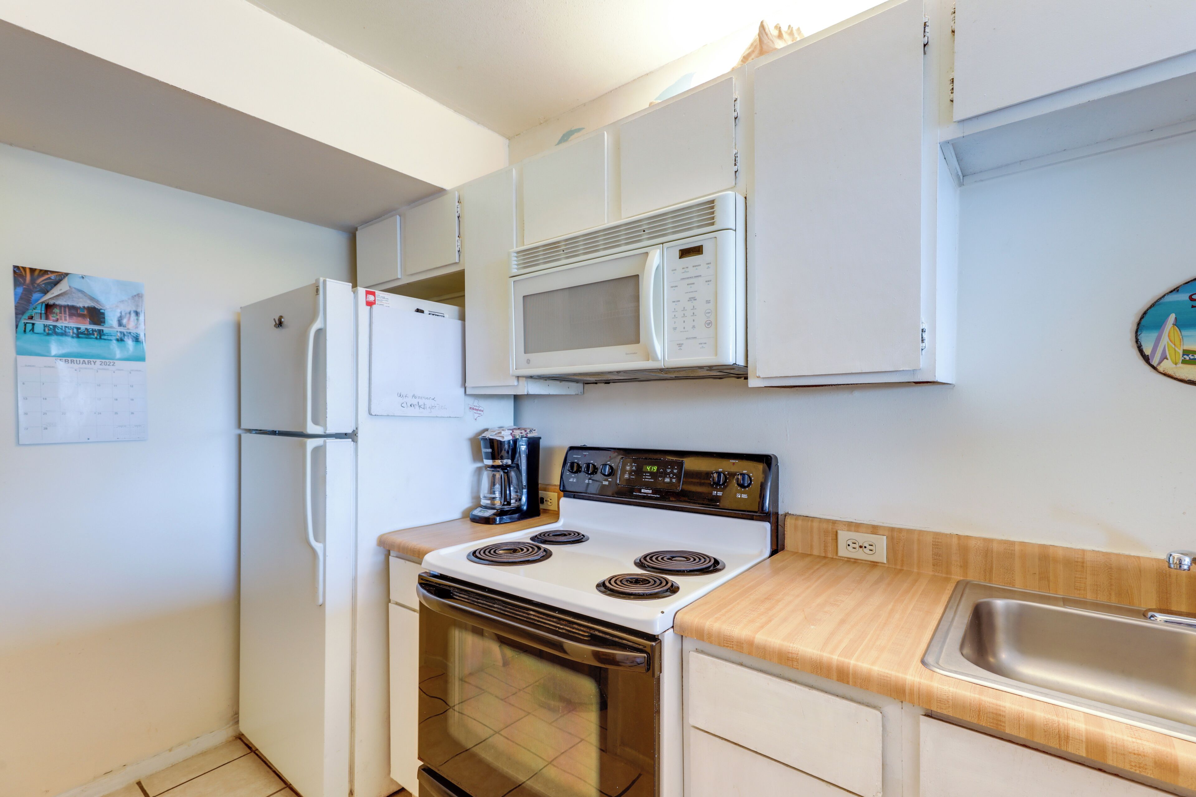 A compact kitchen with a white refrigerator, a microwave, a stove, and a sink.