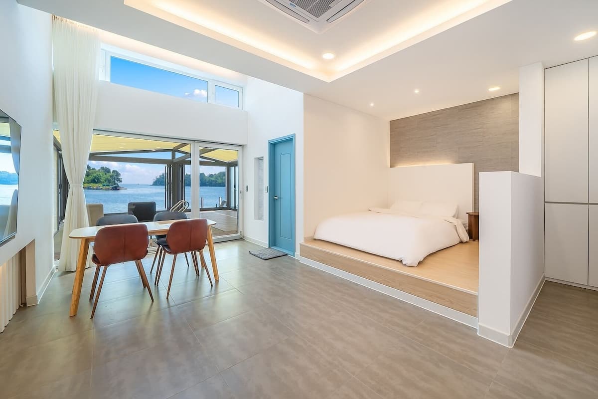 Habitación de hotel moderna con cama, escritorio, sillas y vistas al mar, además de un ventanal grande.