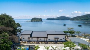 A modern building with a flat roof, a covered outdoor seating area, and a view of a calm lake with boats. - Changwon 055 Poolvilla (Changwon)
