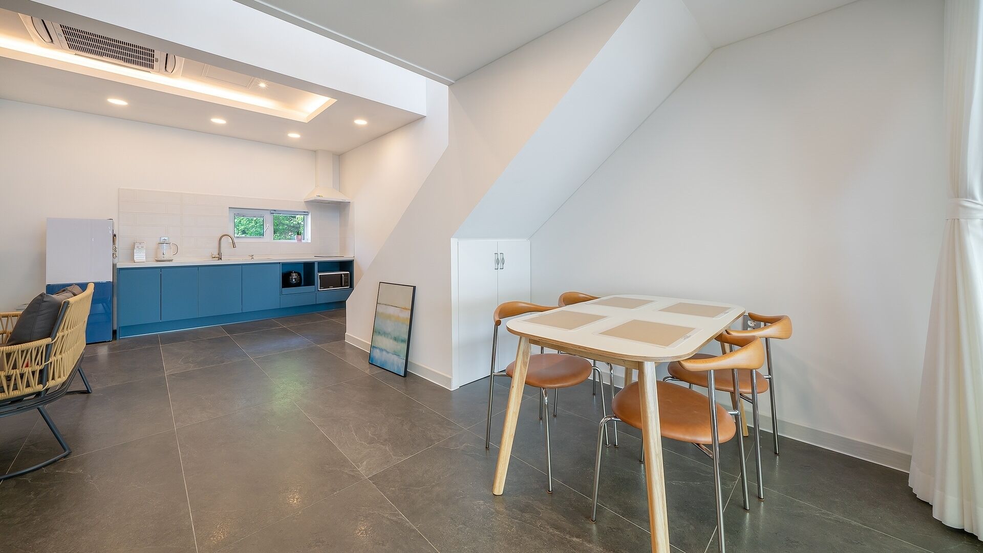 A modern kitchen with blue cabinets, a dining area with a table and chairs, and a white ceiling with recessed lighting.