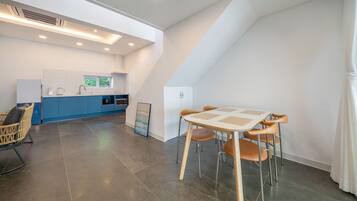 A modern kitchen with blue cabinets, a dining area with a table and chairs, and a white ceiling with recessed lighting.