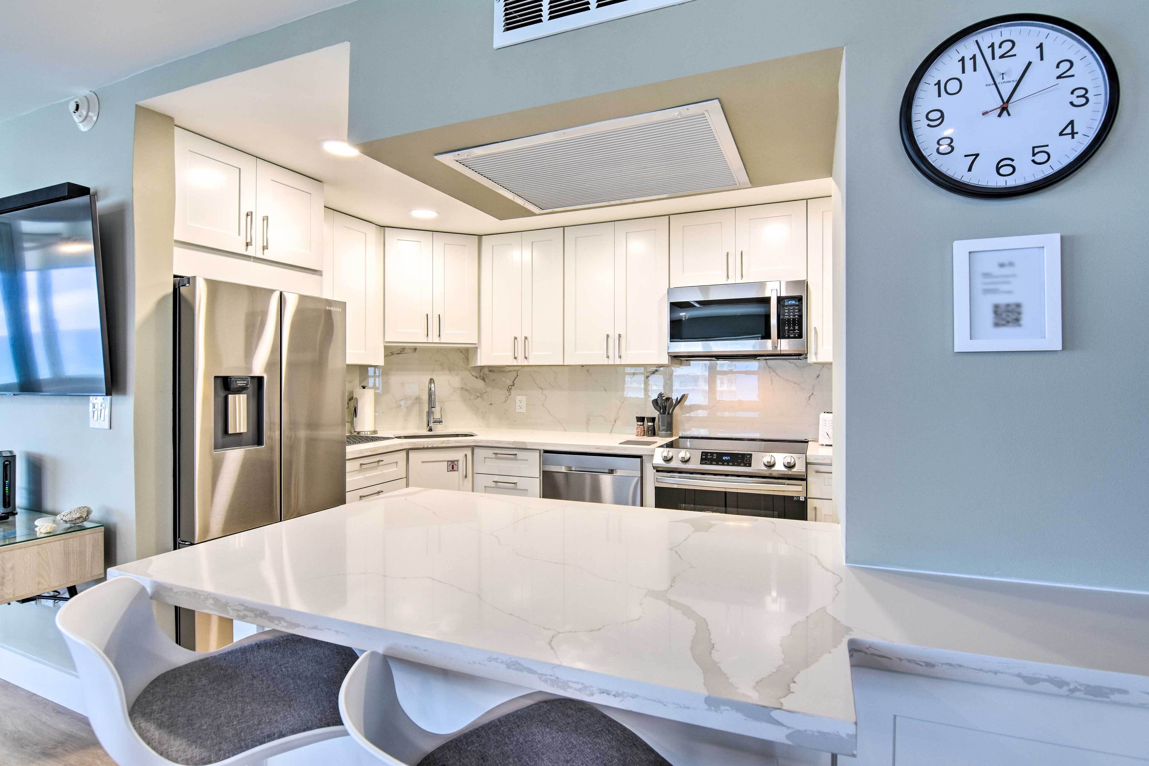 A modern kitchen with white cabinets, stainless steel appliances, and a marble countertop.