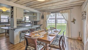 Zona pranzo con tavolo in legno apparecchiato per quattro, cucina con isola integrata e vista su un prato verde attraverso ampie finestre.