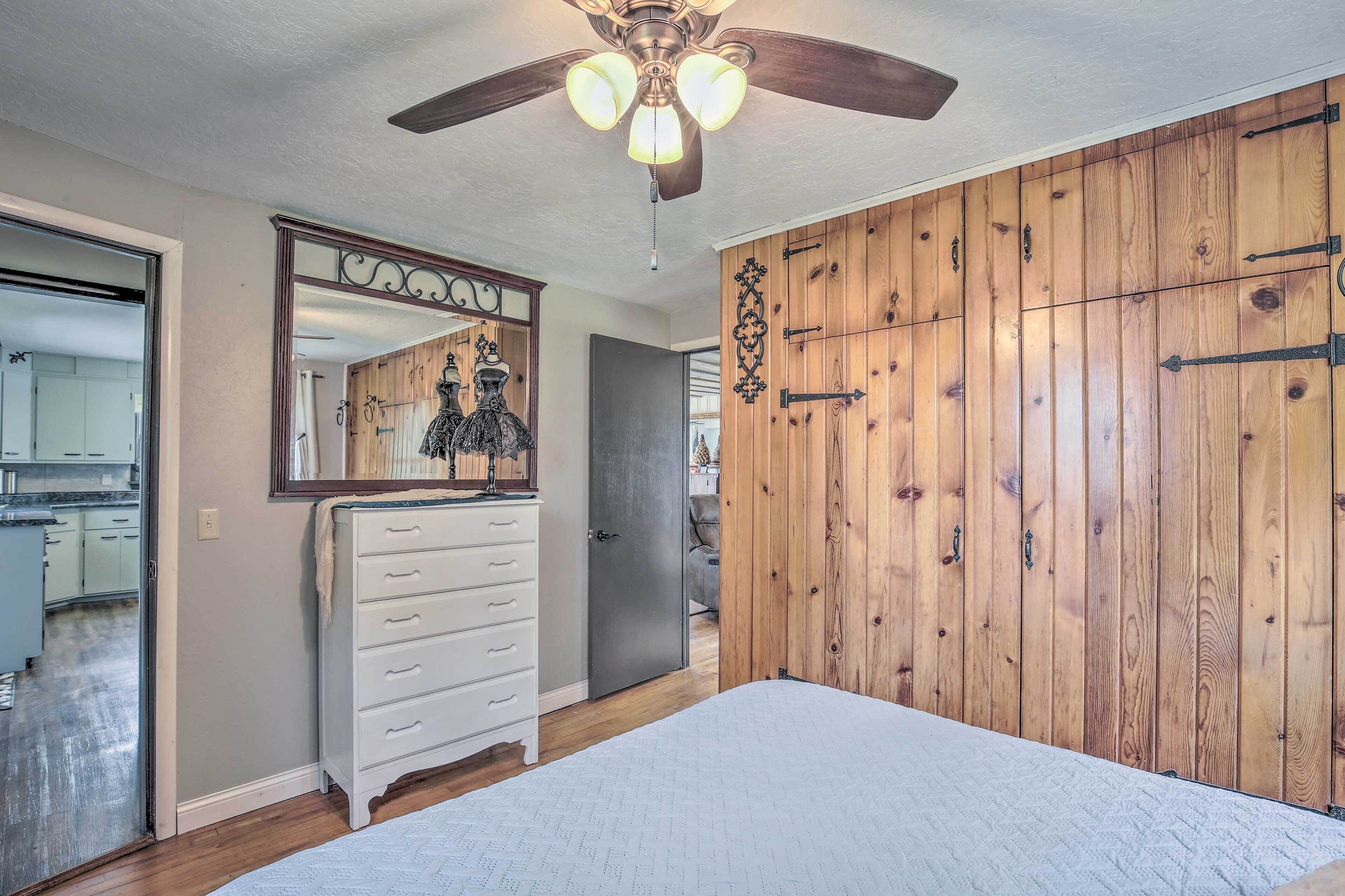 A bedroom with a wooden wardrobe, a white dresser, a ceiling fan, and a large mirror.