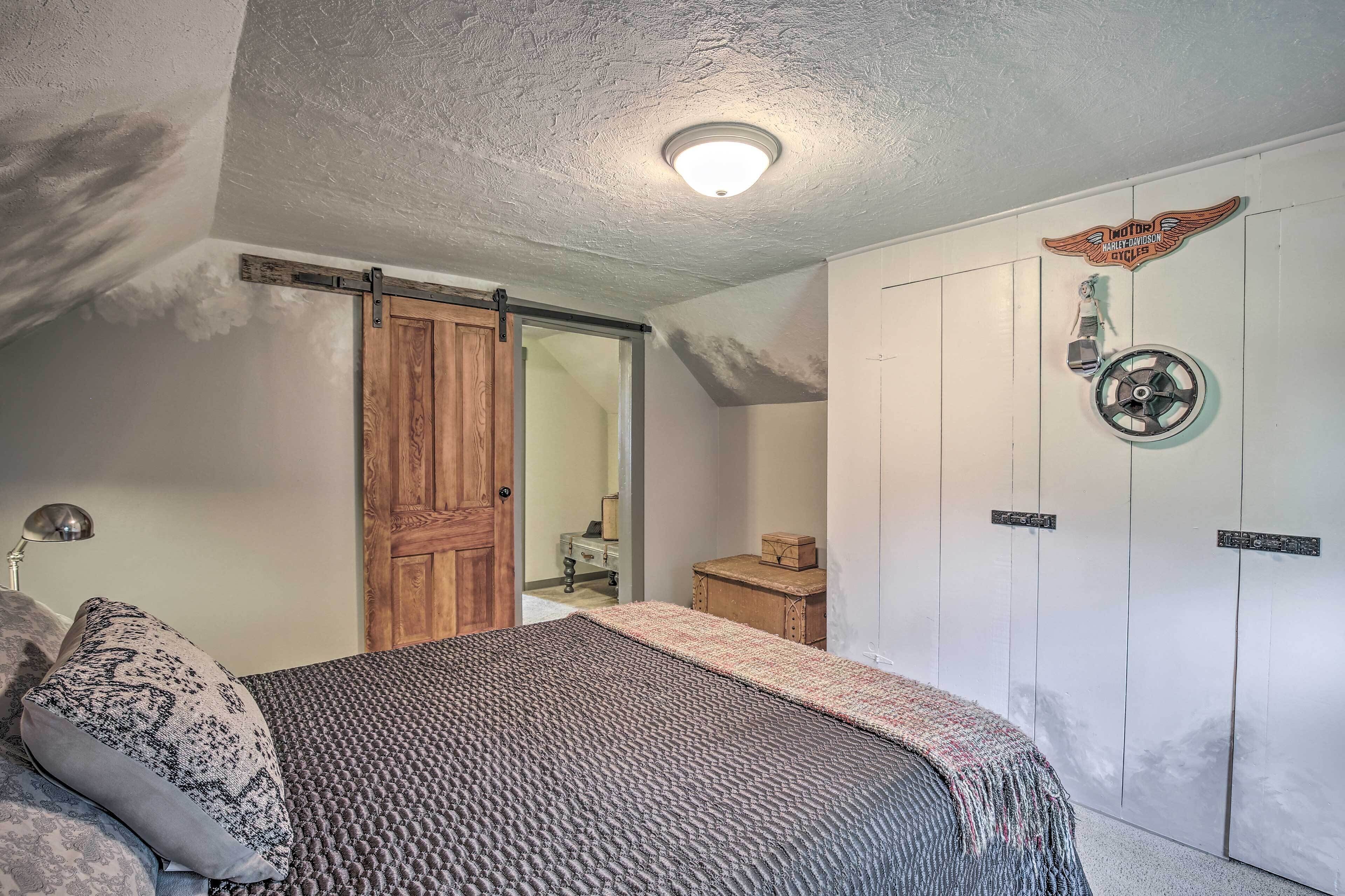 A bedroom with a bed, a wooden door, a ceiling fan, and a wall-mounted light fixture.