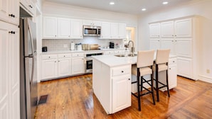A spacious kitchen with white cabinetry, a central island with bar stools, a stainless steel refrigerator, a microwave, and a dishwasher. - 2 Mi to Dtwn: Waco Home w/ Shared Yard! (Waco)