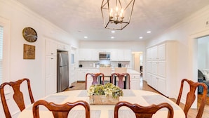 A modern kitchen with white cabinets, a stainless steel refrigerator, and a dining area with wooden chairs and a floral centerpiece. - 2 Mi to Dtwn: Waco Home w/ Shared Yard! (Waco)