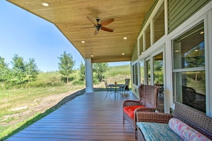 A covered outdoor deck with a ceiling fan, wicker furniture, and large windows overlooking a grassy area. - Lake Home Near Alexandria: Kayaks Provided! (Brandon)