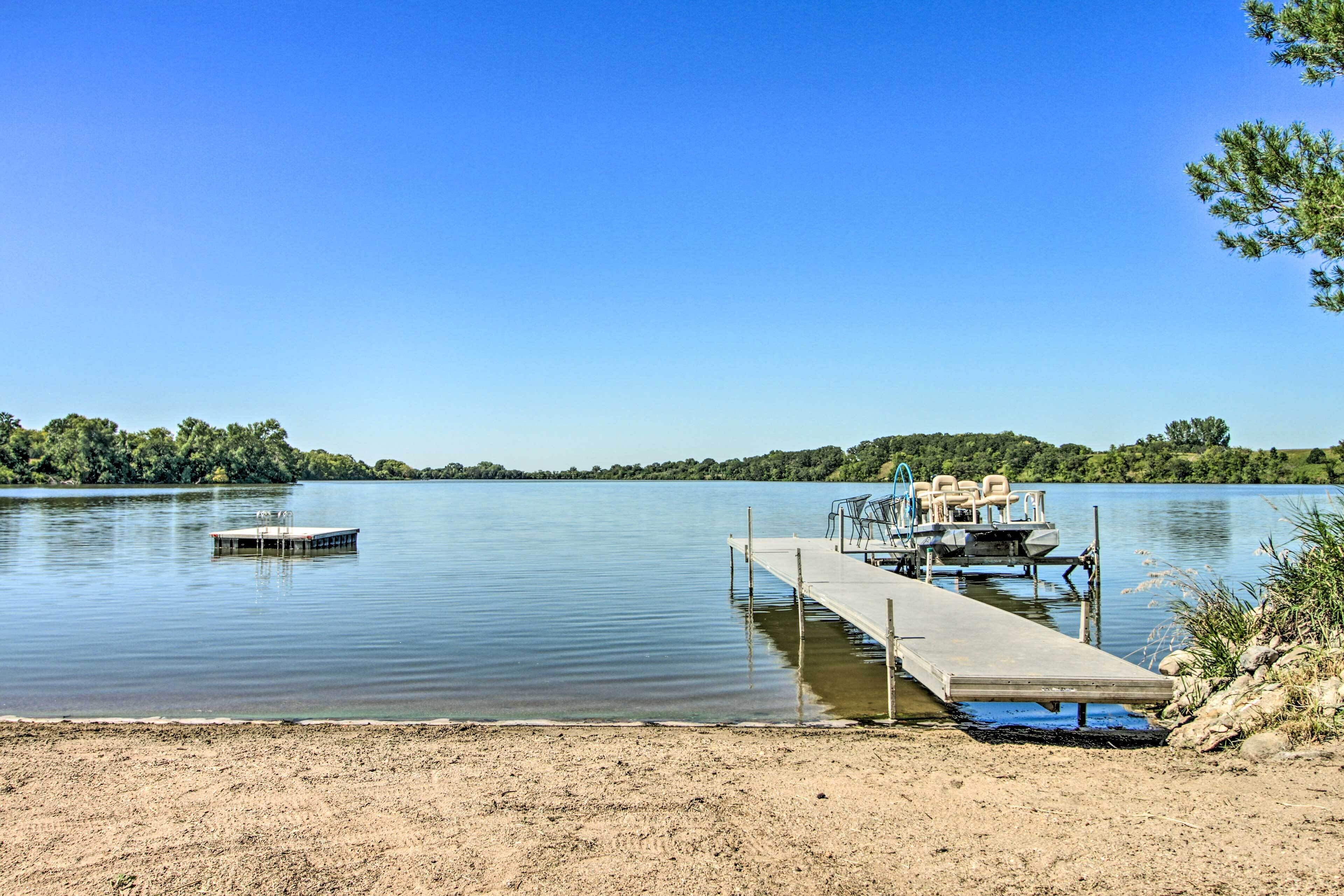 A calm lake with a dock extending into the water, surrounded by greenery.