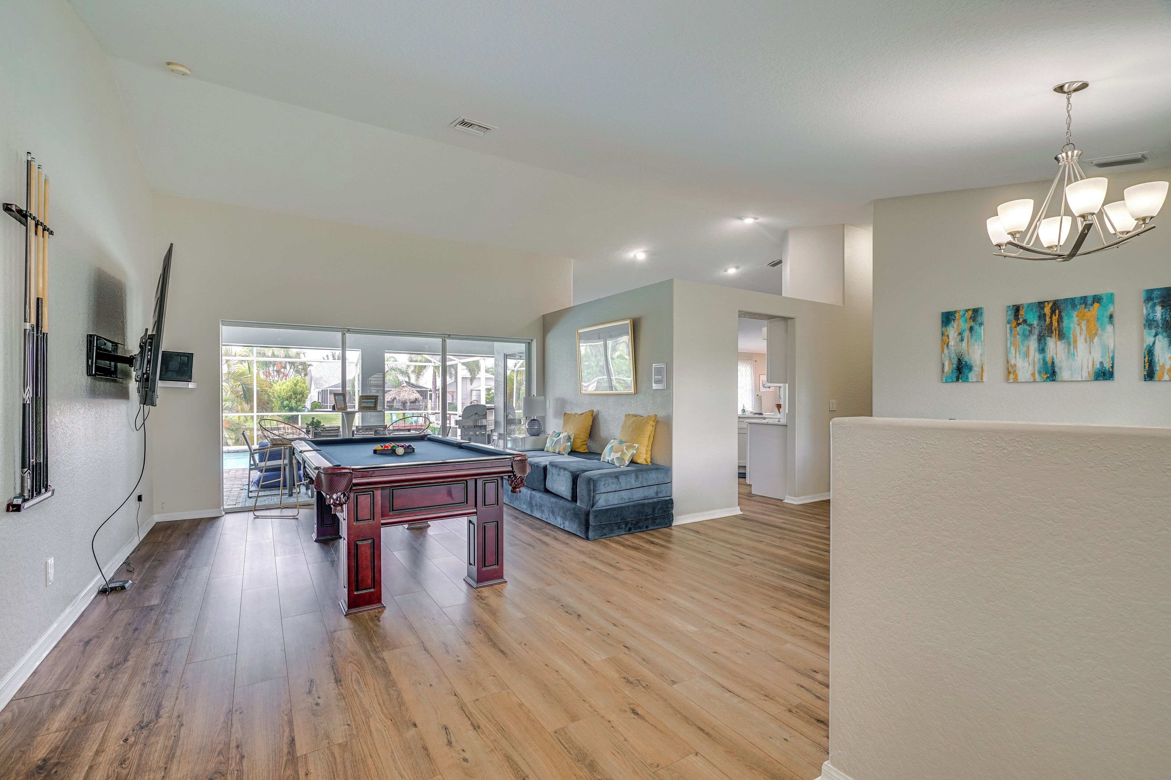 A spacious living room with a pool table, a blue sofa, and a large window offering a view of the outdoors.