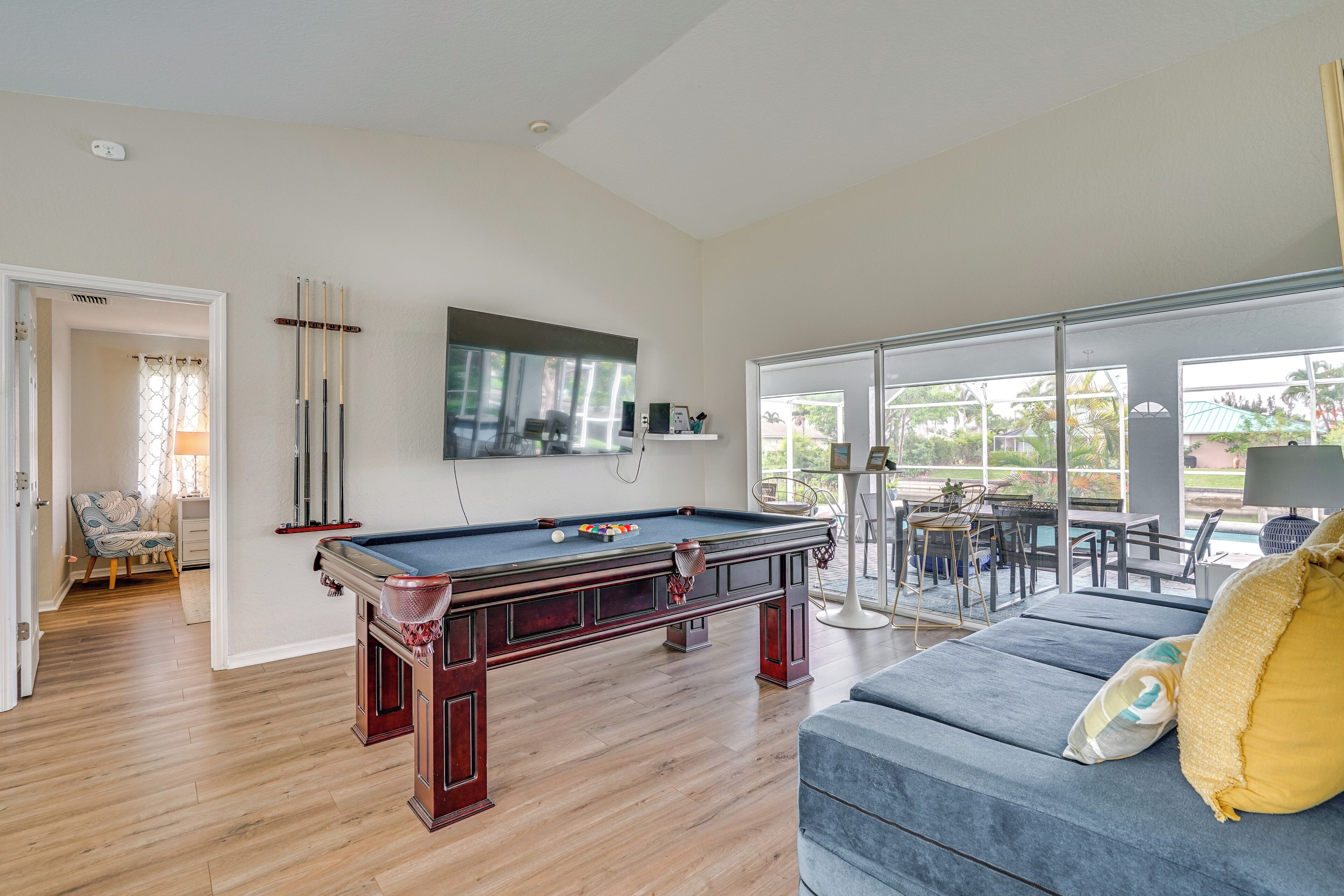 A pool table in a room with a large window, a sofa, and a dining area.