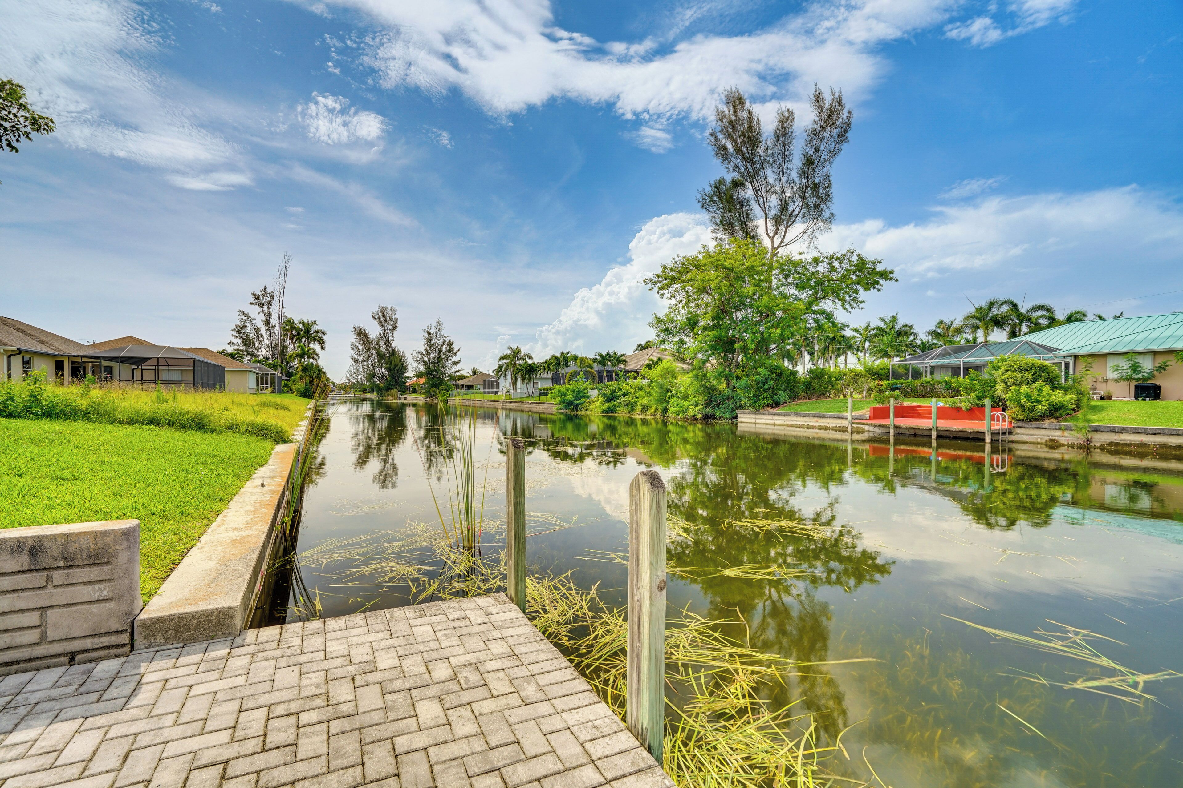 Un canal paisible bordé d’une promenade pavée, entouré d  ’une végétation luxuriante et de bâtiments résidentiels.