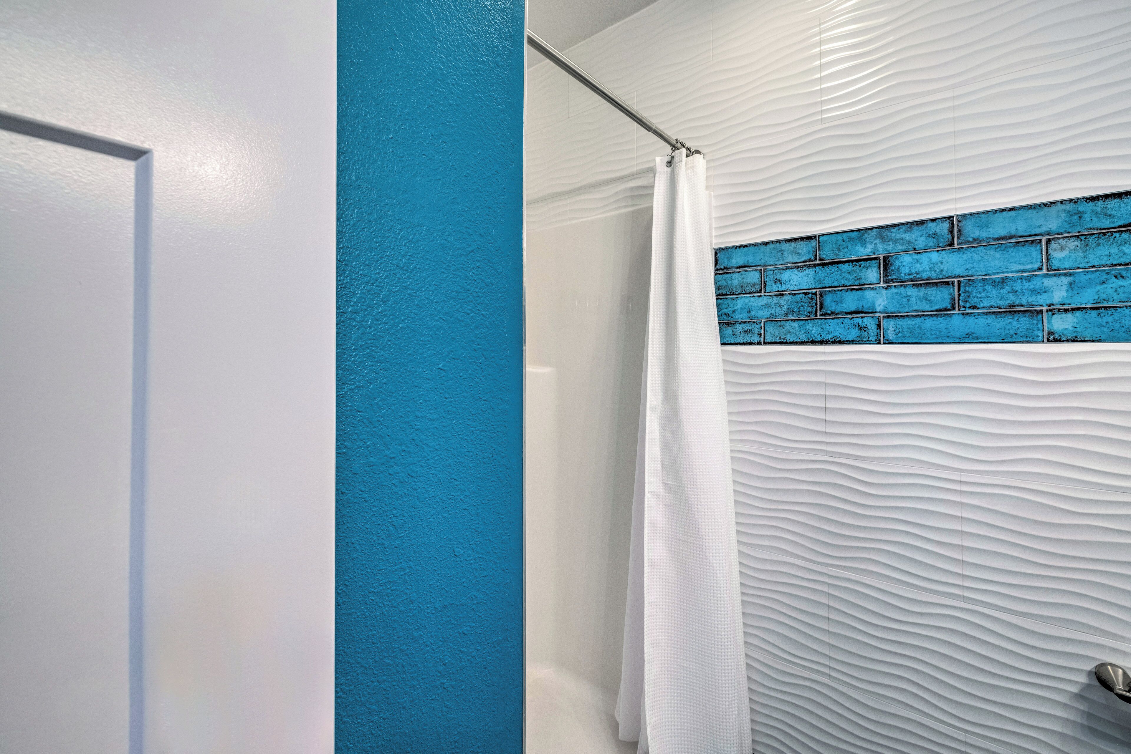 Une salle de bain avec un mur blanc à texture, un mur d’accent bleu et un rideau de douche.