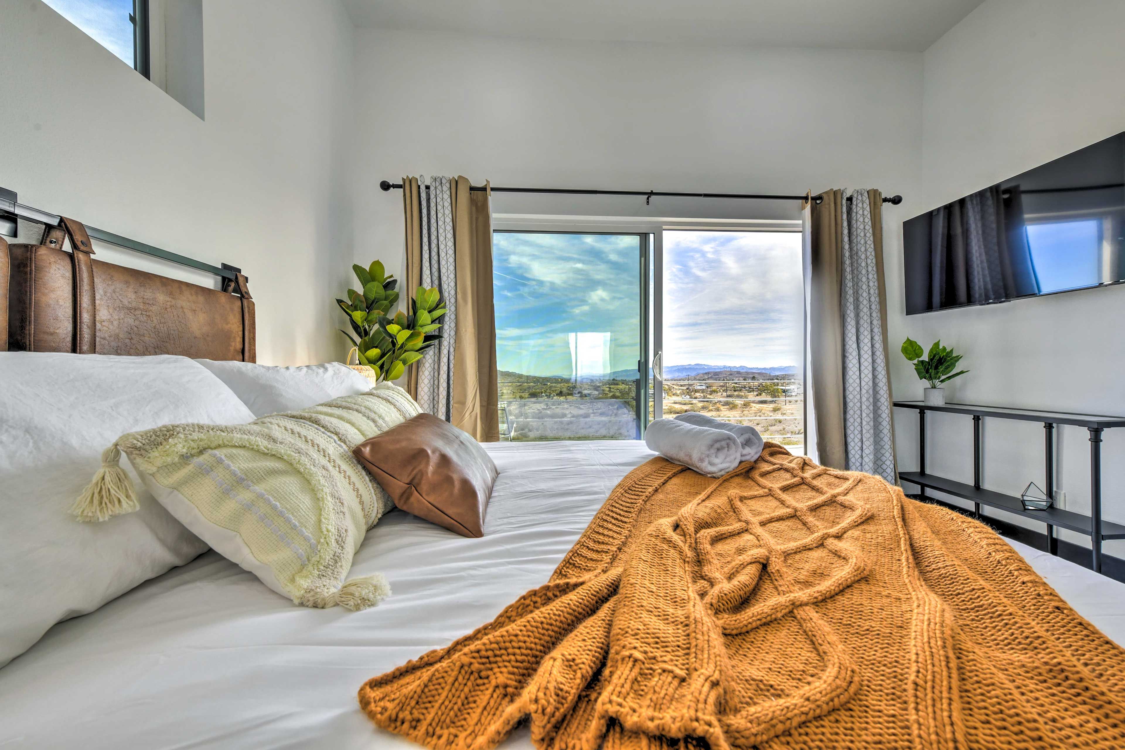 Een slaapkamer met een bed, een raam met gordijnen, een aan de muur bevestigde televisie en een plant.