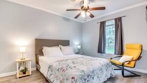 Ein Schlafzimmer mit Bett, Nachttisch, Stuhl, Deckenventilator und einem Fenster mit Vorhängen.