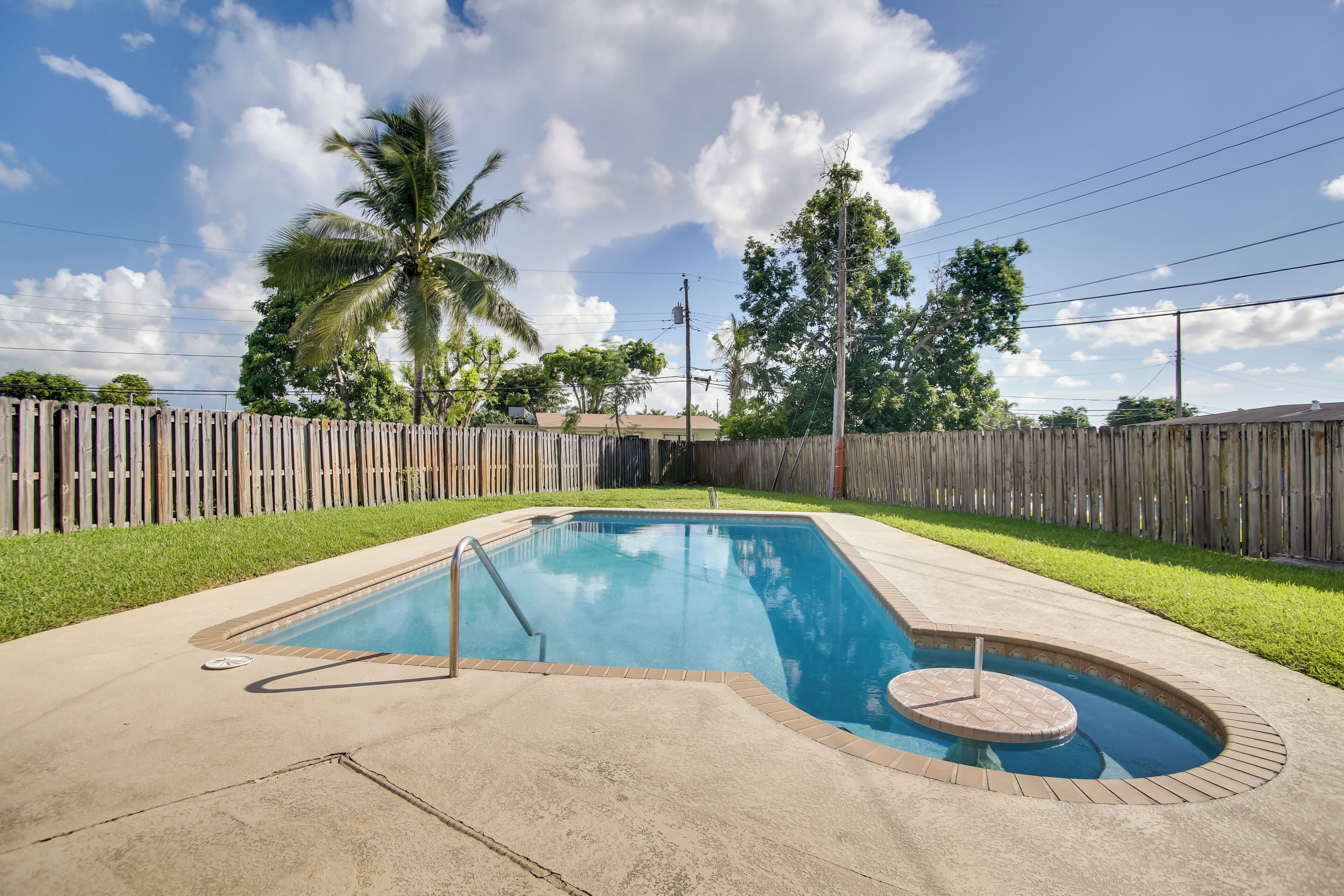 Une piscine rectangulaire bordée de briques et dotée d’un espace jacuzzi circulaire, le tout entouré d’une clôture en bois et de verdure.