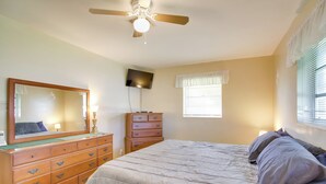 Ein Schlafzimmer mit Bett, Kommode, Spiegel, Deckenventilator und Fenster mit Jalousien.