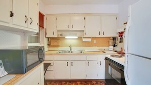 Eine kleine Küche mit weißen Schränken, einer Mikrowelle, einem Spülbecken und einem Kühlschrank.
