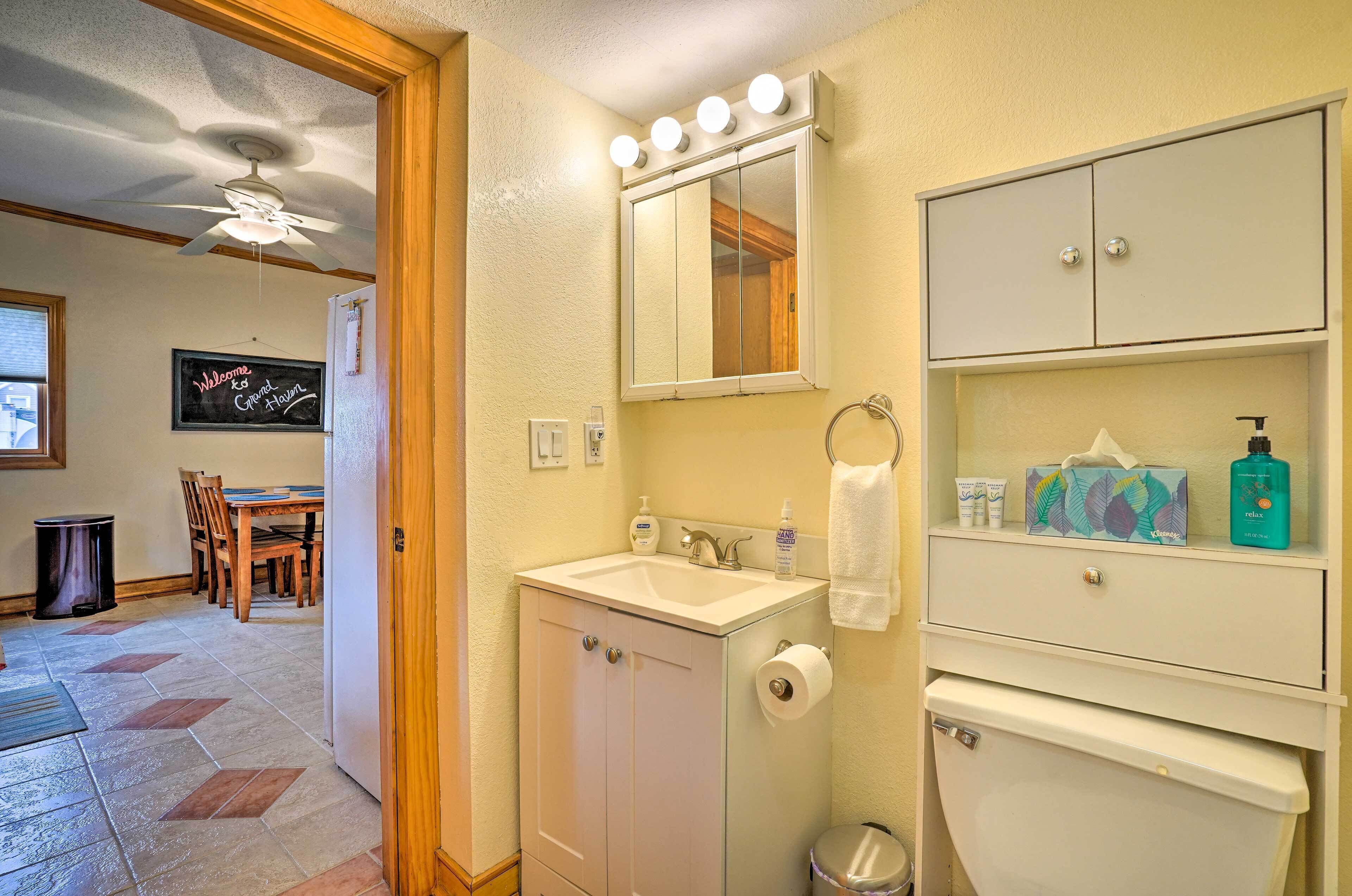 A bathroom with a sink, mirror, and toiletries. There is a door leading to a dining area.