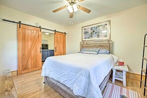 Une chambre à coucher avec un lit, une armoire en bois, un ventilateur de plafond, un tableau encadré et une table de chevet.