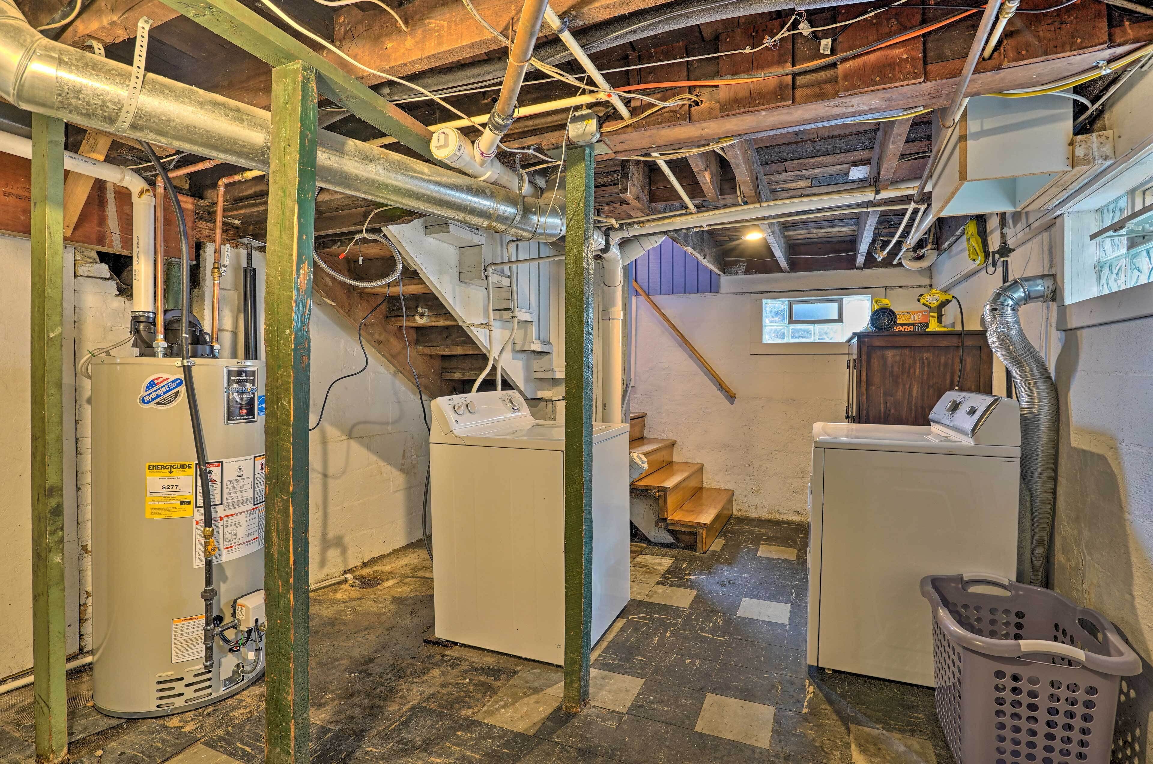 A basement with a water heater, washing machine, and laundry basket.